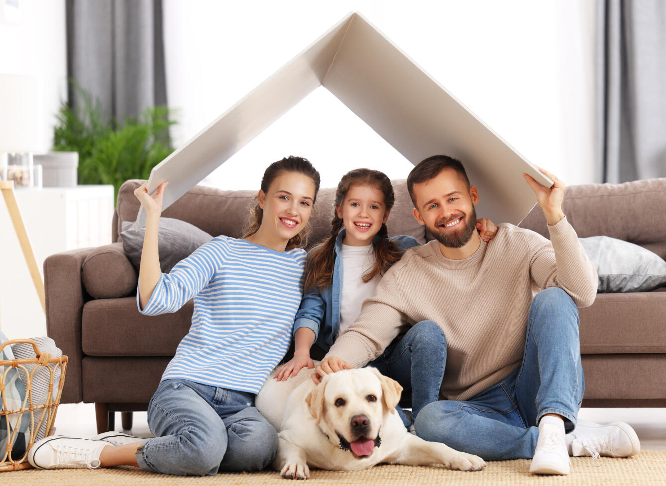 Family sitting on the floor with a dog, holding a board above their heads like a roof over their heads, simulating safe and protection.